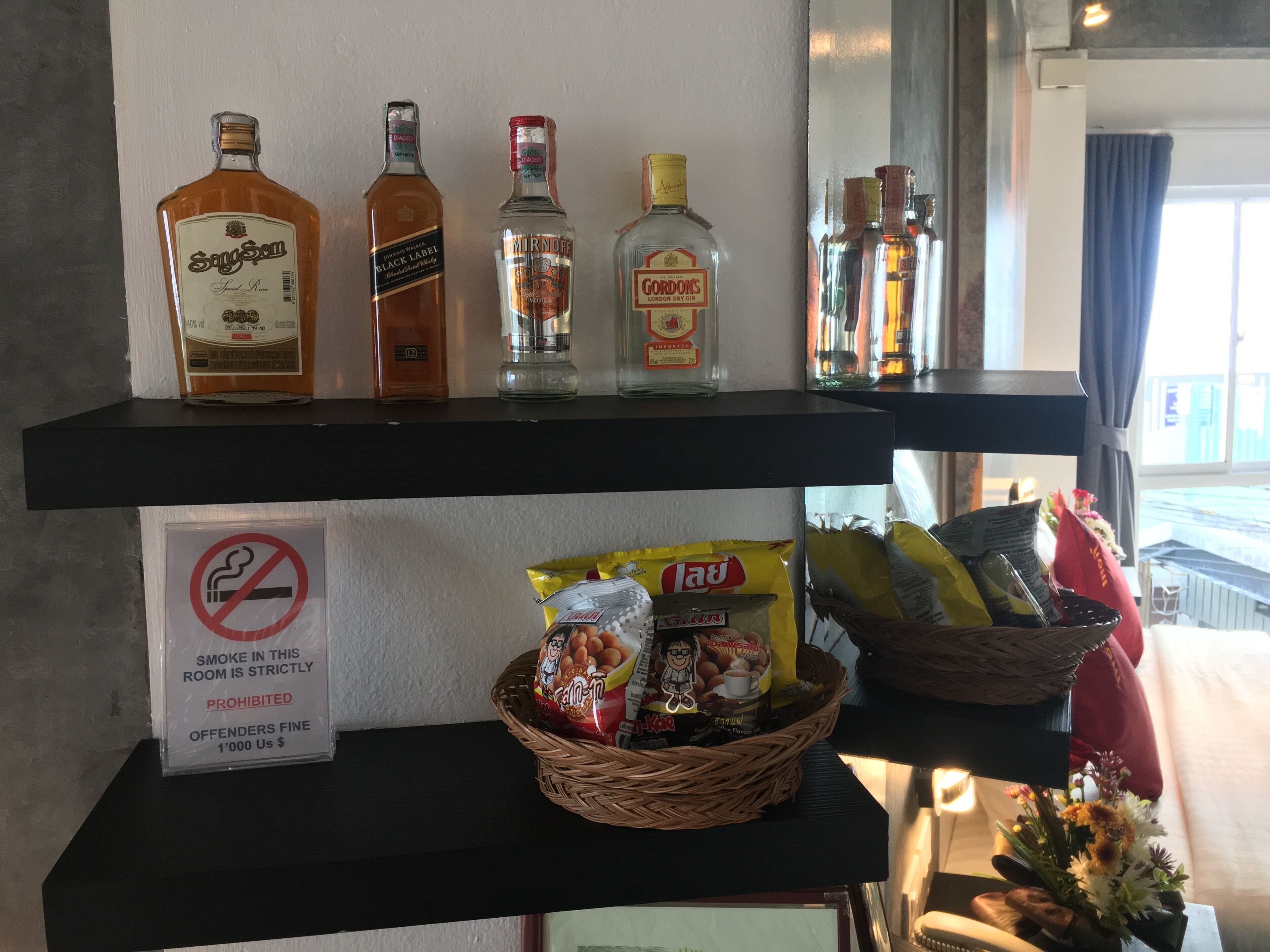 A shelf with various liquor bottles, a no-smoking sign, and a basket of snacks.
