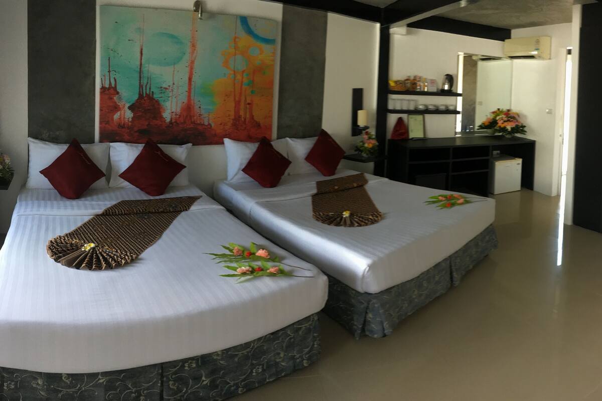 Habitación de hotel con dos camas, un cuadro abstracto grande, una pequeña zona de cocina y un baño visible a través de una puerta abierta.