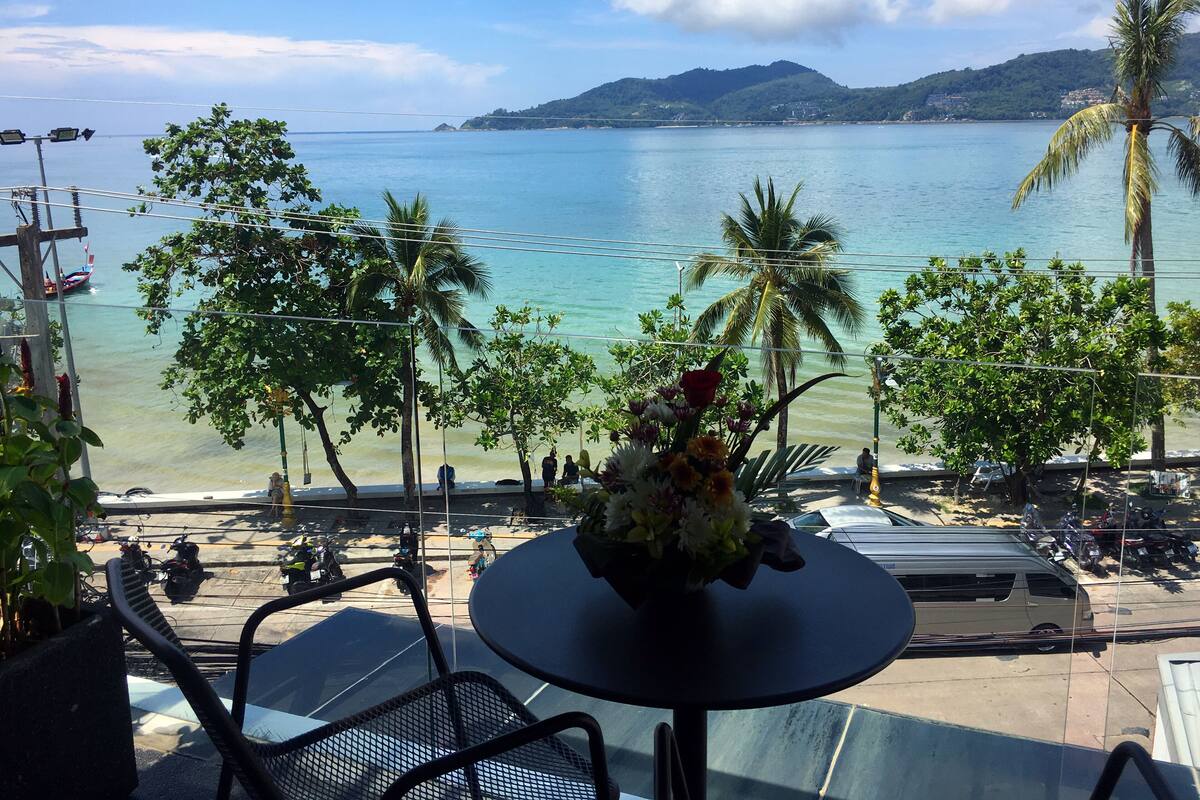 Una mesa con un arreglo floral, con vista a una playa con palmeras y la vista del mar y colinas al fondo.