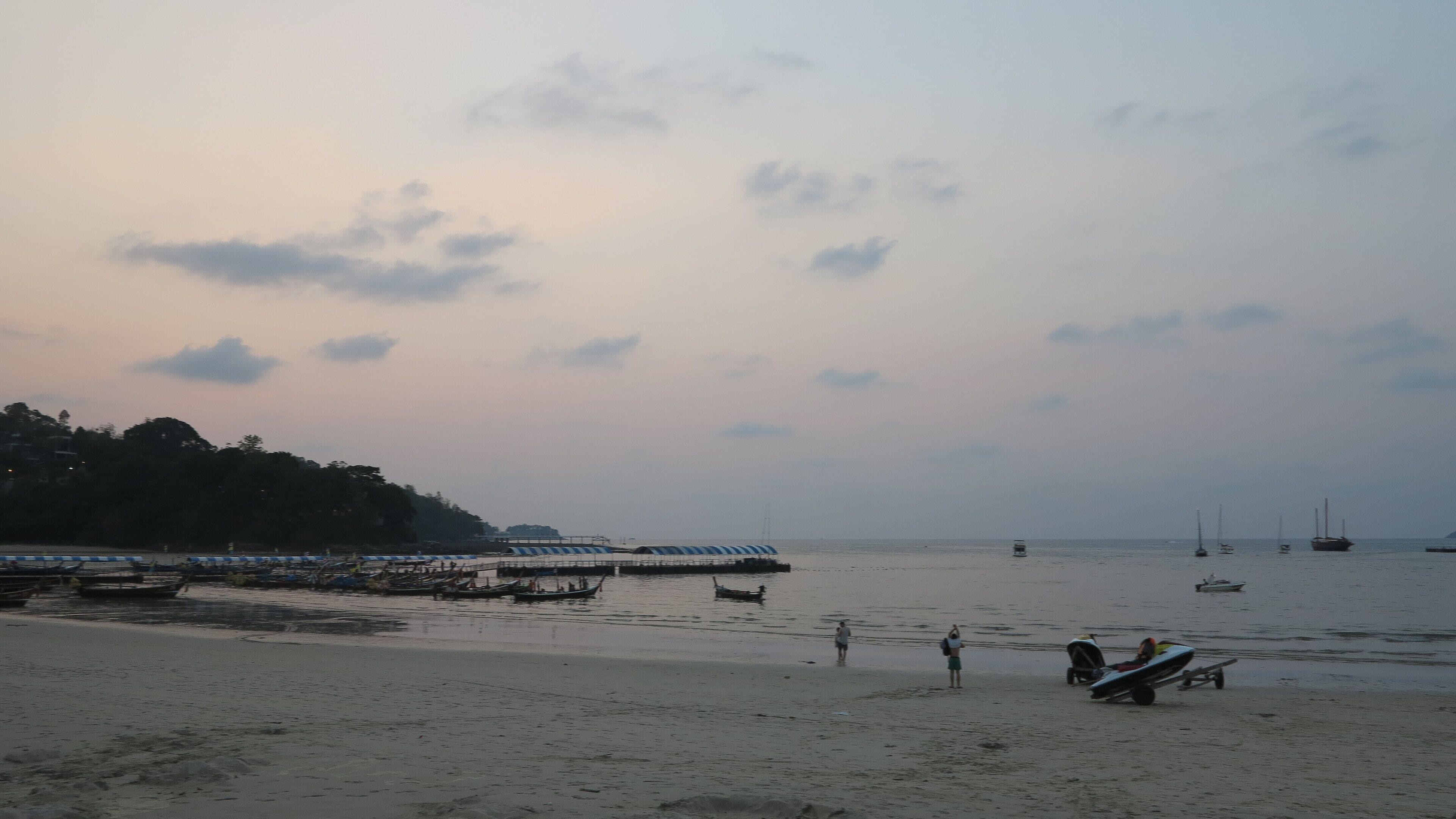 A beach with boats and a pier.