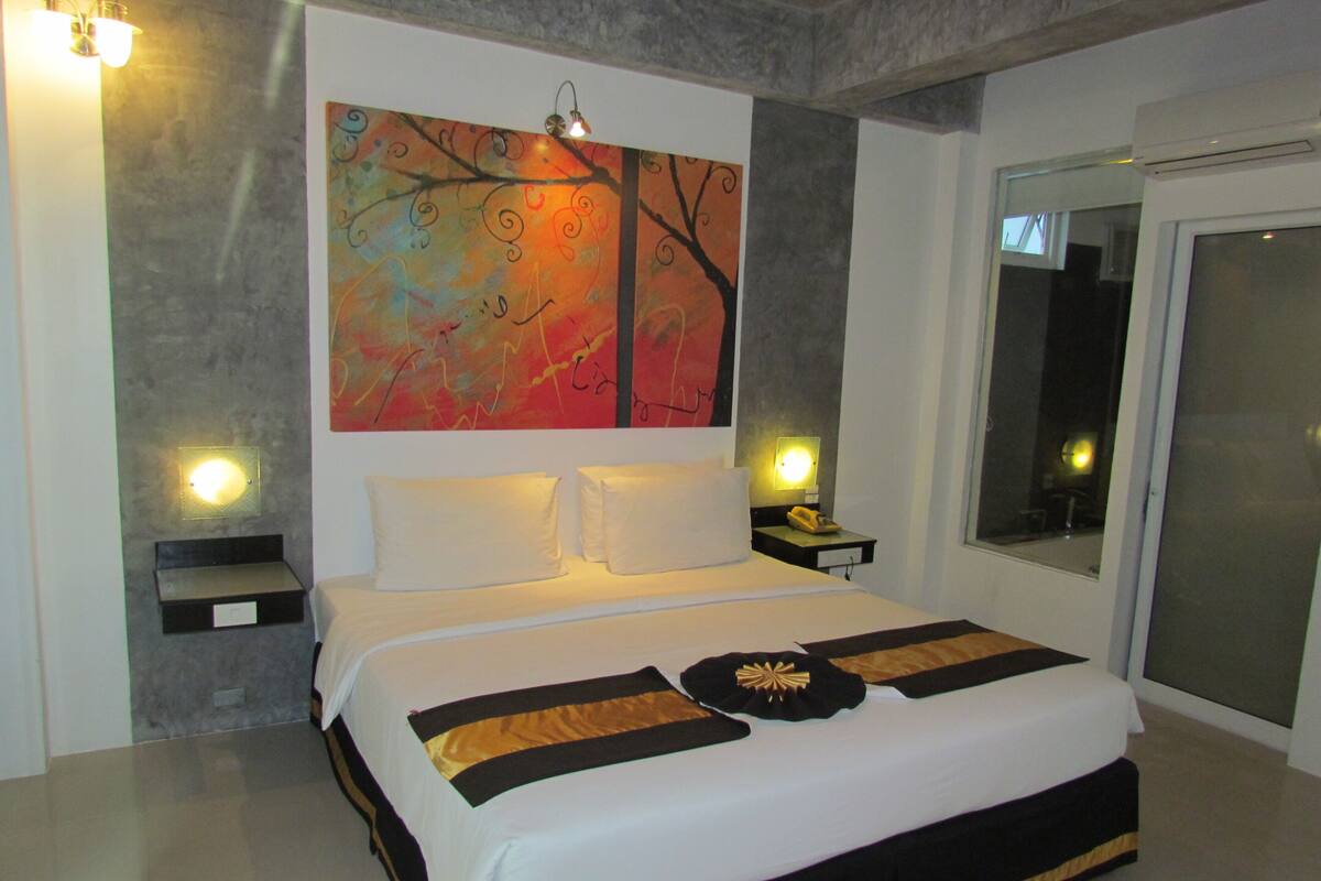 Una habitación de hotel moderna con una cama grande, un cuadro en la pared y una mesita de noche con una lámpara.
