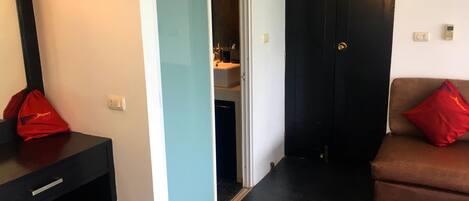 Ein Zimmer mit einem schwarzen Schreibtisch, einer roten Tasche, einem braunen Sofa mit rotem Kissen und einer Tür zu einem Badezimmer.