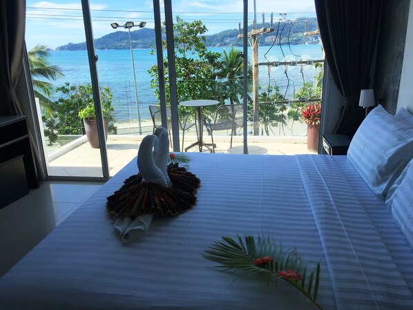 A hotel room with a bed, a view of the sea, and a balcony with a table and chairs. - The Front Hotel and Apartment (Patong)