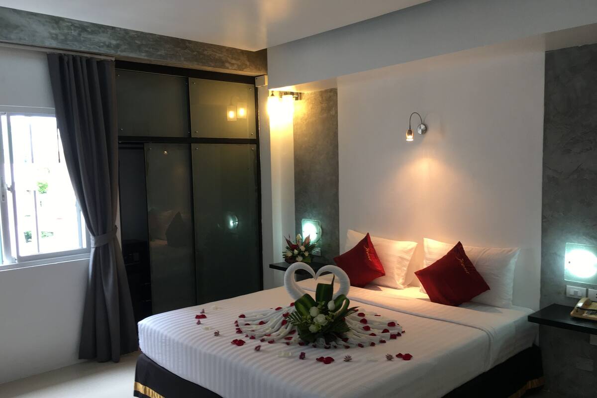 Una cama bien hecha con ropa blanca, almohadas rojas y una decoración central con forma de cisne.