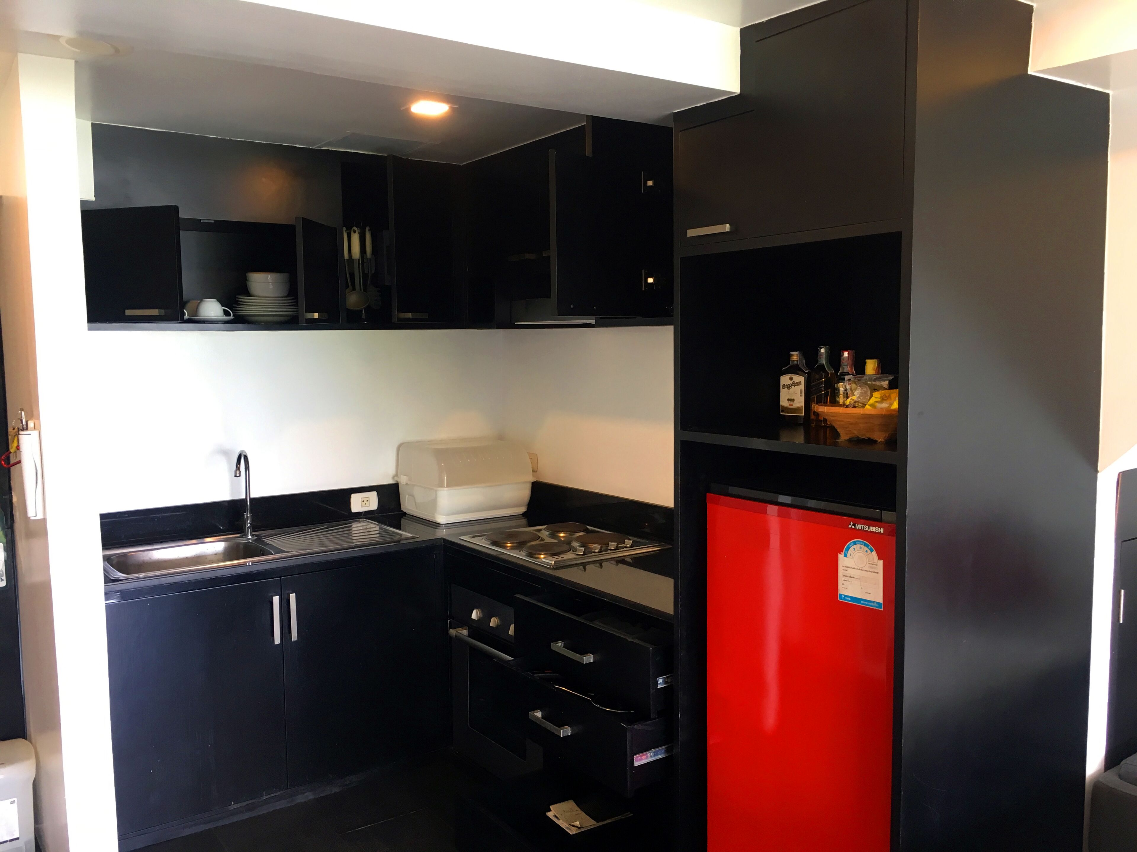 Una cocina compacta con armarios negros, un refrigerador rojo, un lavamanos y un microondas.