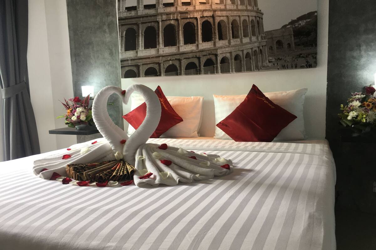 Habitación de hotel con cama decorada con un arreglo de toallas con forma de cisne, ropa de cama a rayas y almohadas rojas.