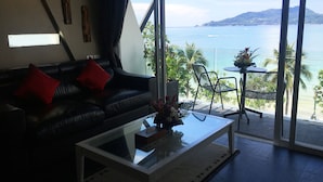 A modern living room with a leather sofa, a glass coffee table, and a view of the ocean. - The Front Hotel and Apartment (Patong)