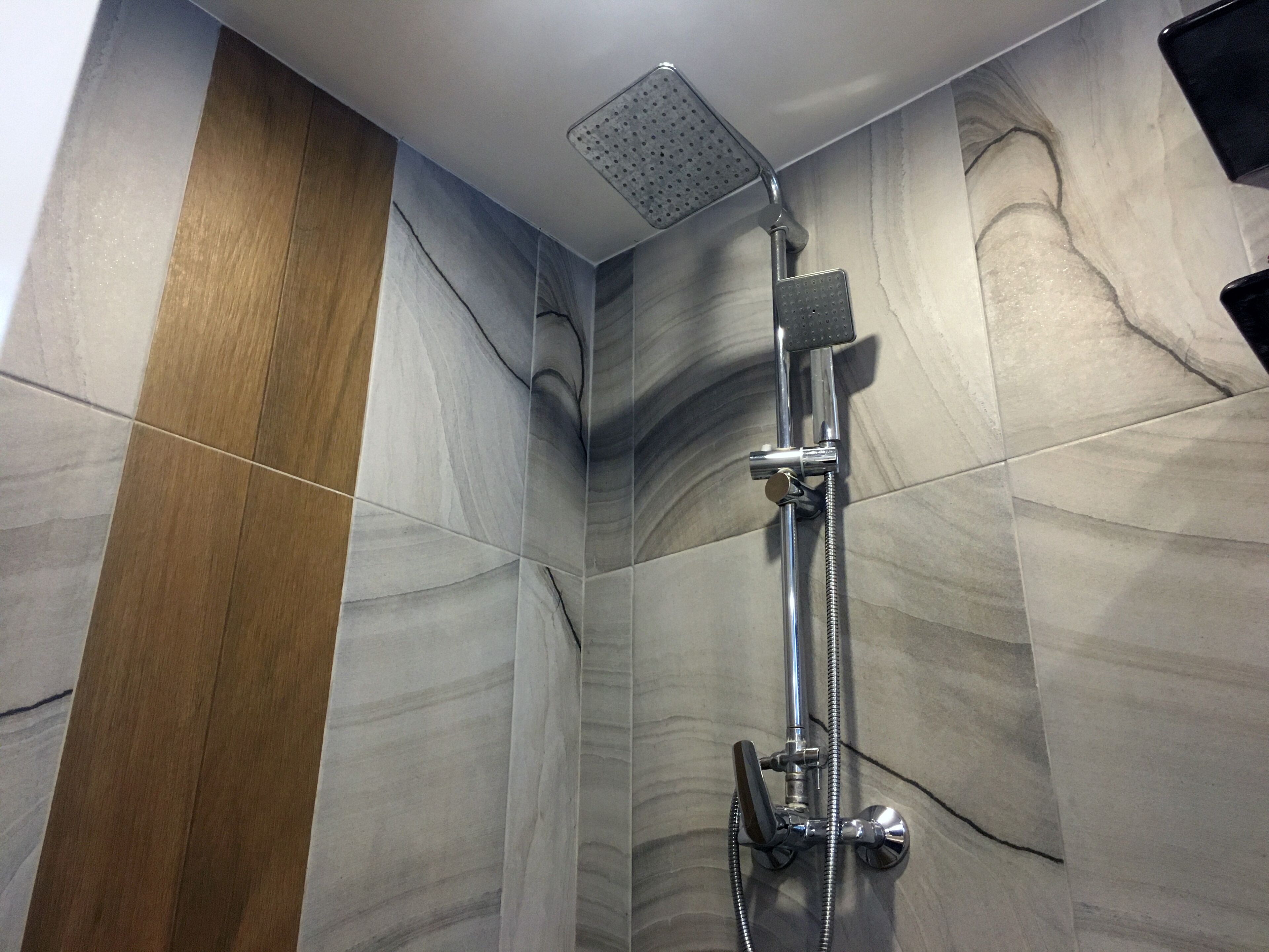 A shower with a handheld showerhead and a fixed showerhead, both mounted on a wall with a marble-like tile pattern.