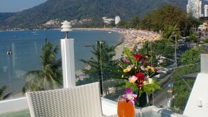 A table with a magazine, a glass of orange drink, and a flower arrangement. - The Front Hotel and Apartment (Patong)