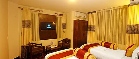 Habitación de hotel con dos camas, un escritorio con silla, un televisor y cortinas.