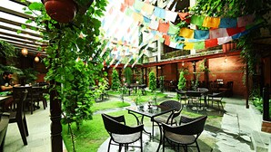 Zona pranzo all'aperto con tavoli e sedie, immersa nel verde e circondata da muri in mattoni.