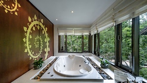 A modern bathroom with a large bathtub, a window with a view of greenery, and decorative wall art. - Suuko Villas (Chalong)