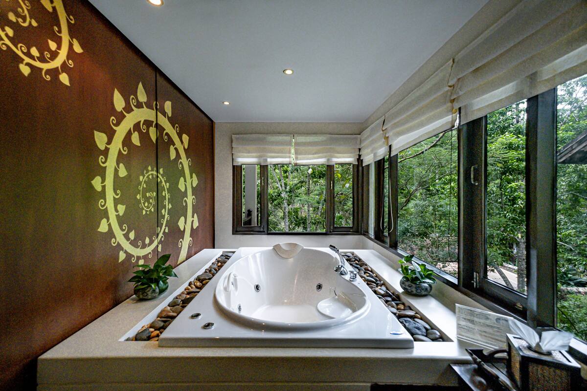 Un baño moderno con una bañera grande, una ventana con vistas a la vegetación y decoración en la pared.