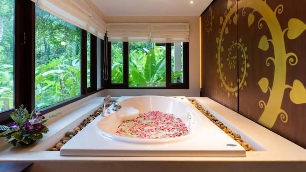 A modern bathroom with a large bathtub, a window with a view of greenery, and decorative wall art. - Suuko Villas (Chalong)