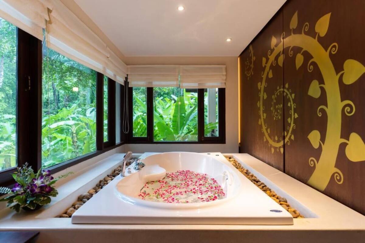 Un baño moderno con una bañera grande, una ventana con vistas a la vegetación y decoración mural.
