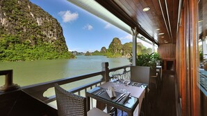 A dining area with tables and chairs, overlooking a river with cliffs. - Paradise Peak Cruise (Tuan Chau)