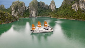 A boat with multiple sails on a calm river surrounded by rocky cliffs.