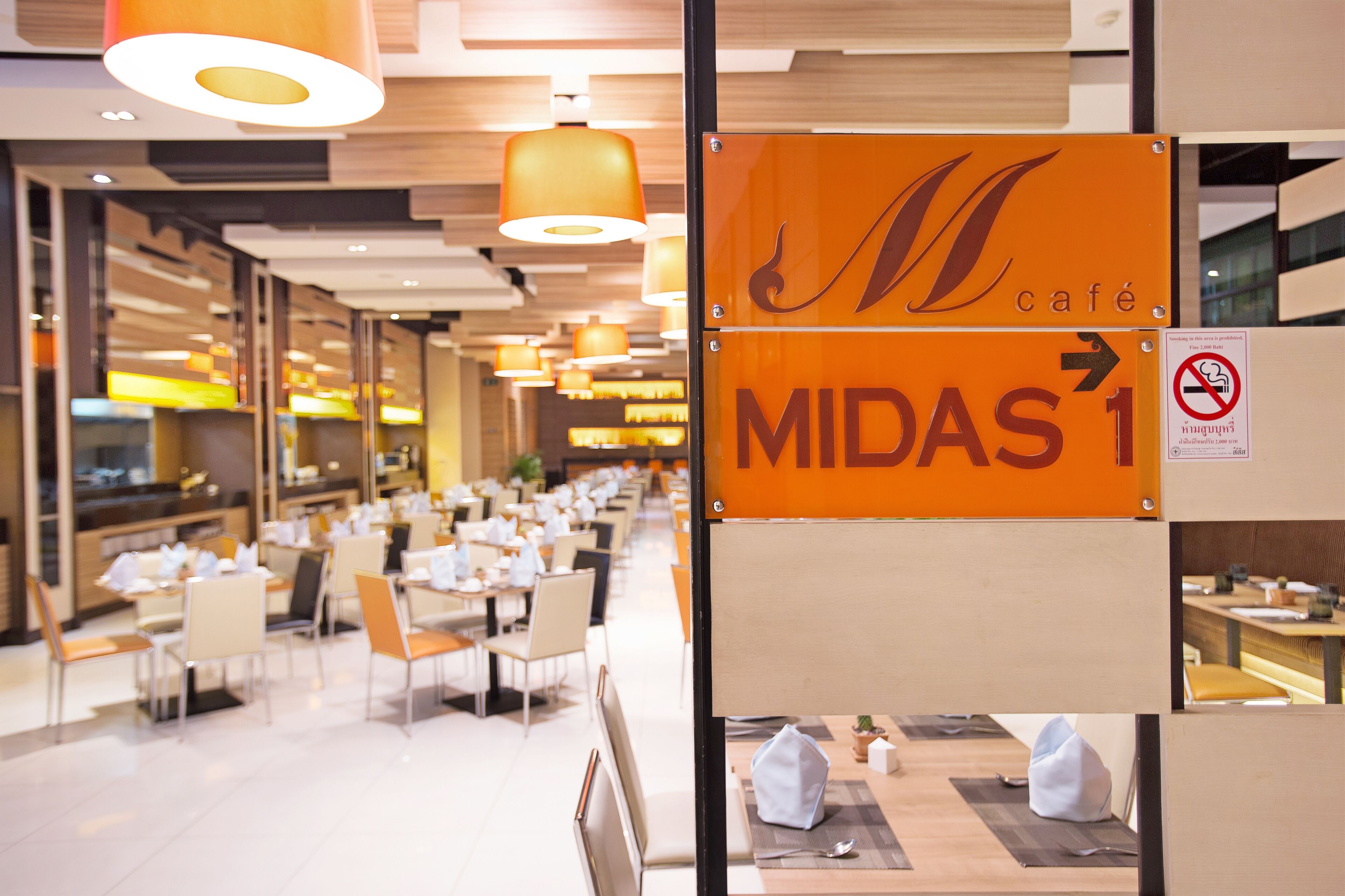 A modern dining area with tables and chairs, a sign indicating 'Midas Café', and a directional sign pointing to the right.