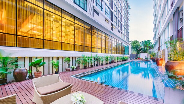 A modern hotel with a swimming pool, outdoor seating, and potted plants. - Mida Hotel Ngamwongwan (Nonthaburi)