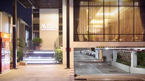 A hotel entrance with a modern design, a staircase leading to the lobby, and a parking area with cars. - Mida Hotel Ngamwongwan (Nonthaburi)