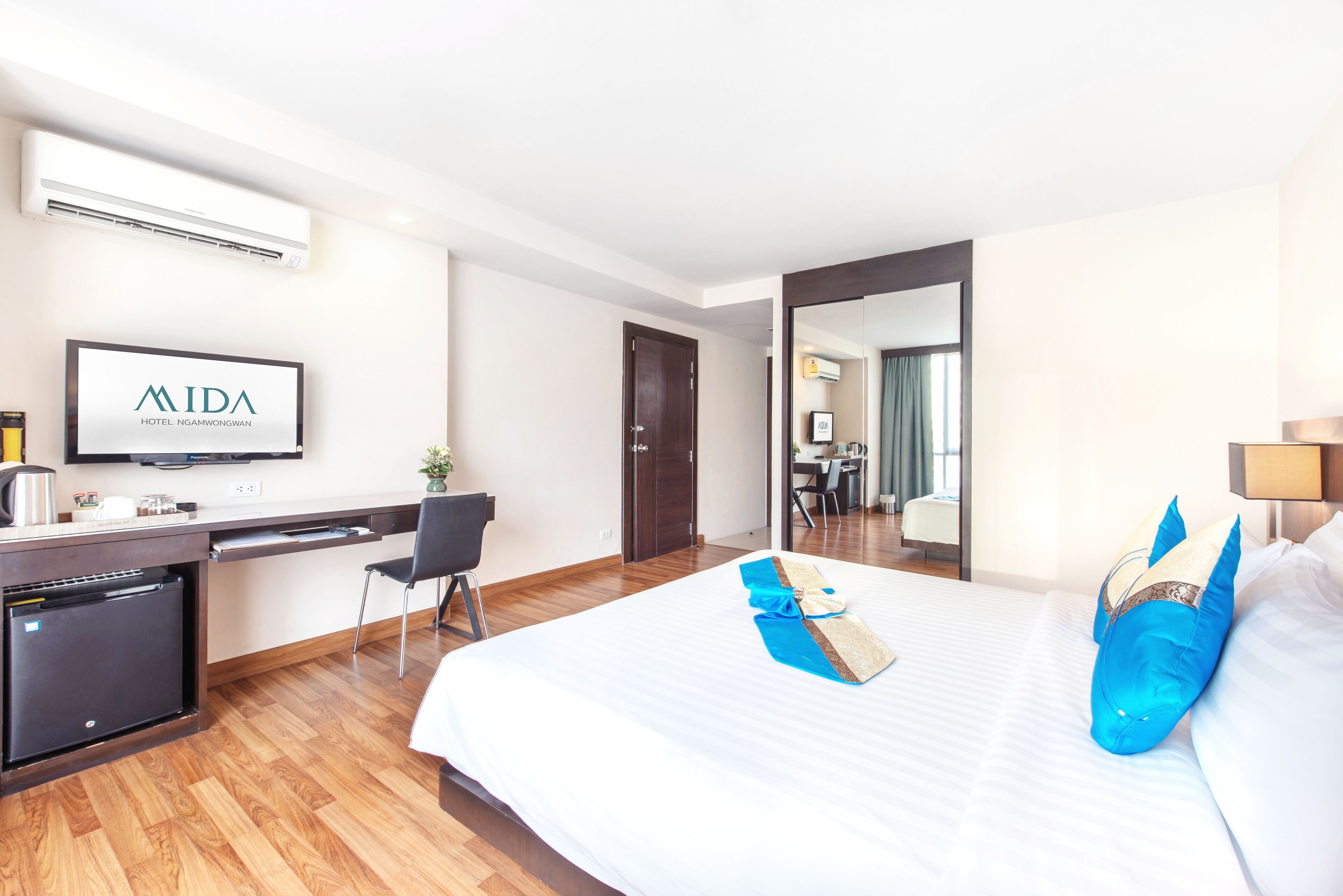 A hotel room with a bed, a desk, a chair, a TV, and a minibar.