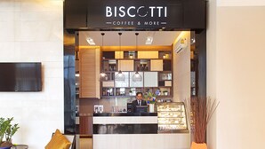 A modern coffee shop interior with a counter, shelves with products, and a seating area with chairs and a table. - Mida Hotel Ngamwongwan (Nonthaburi)