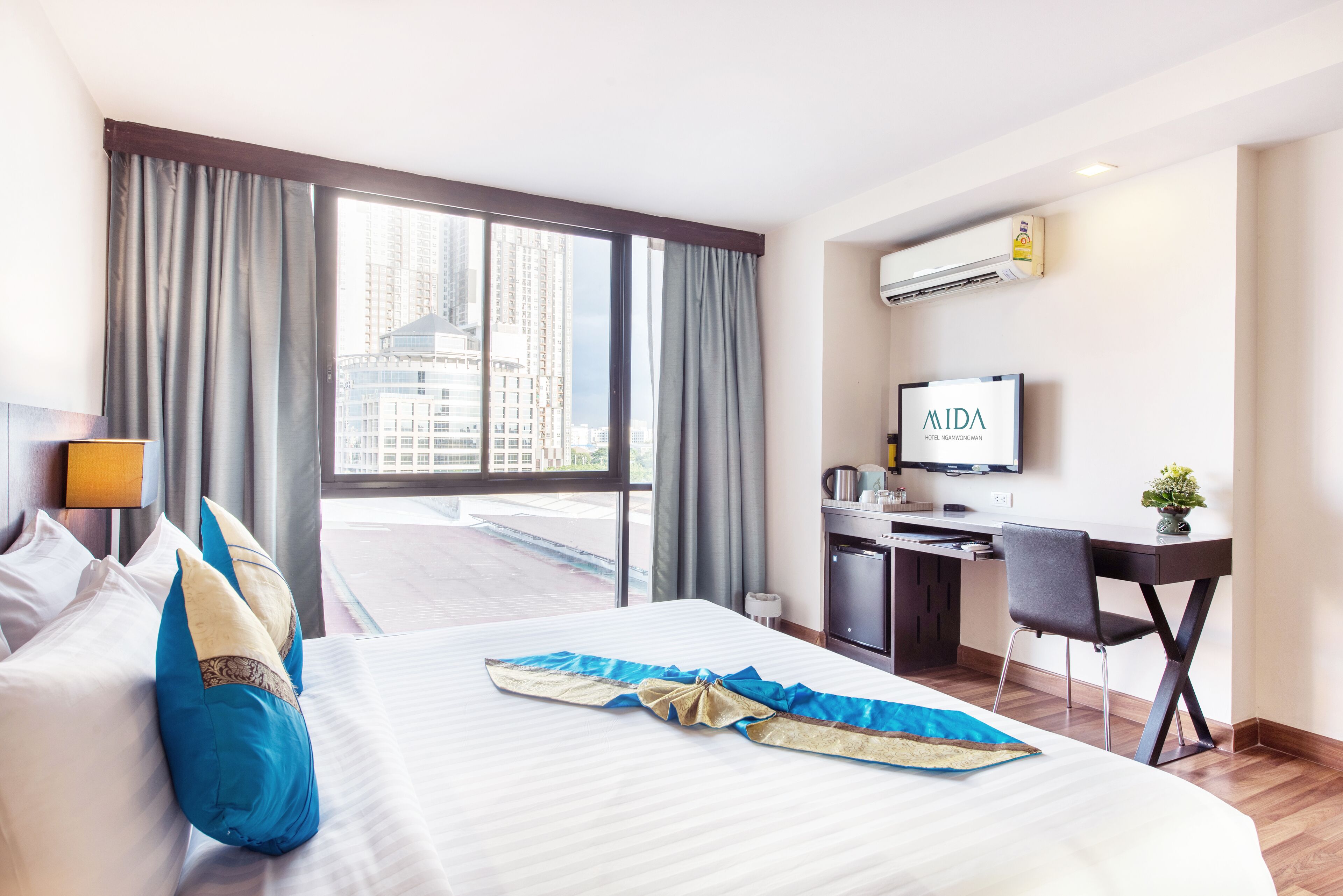 Una camera d'hotel con un letto, una scrivania, una sedia, una televisione e una finestra con tende.