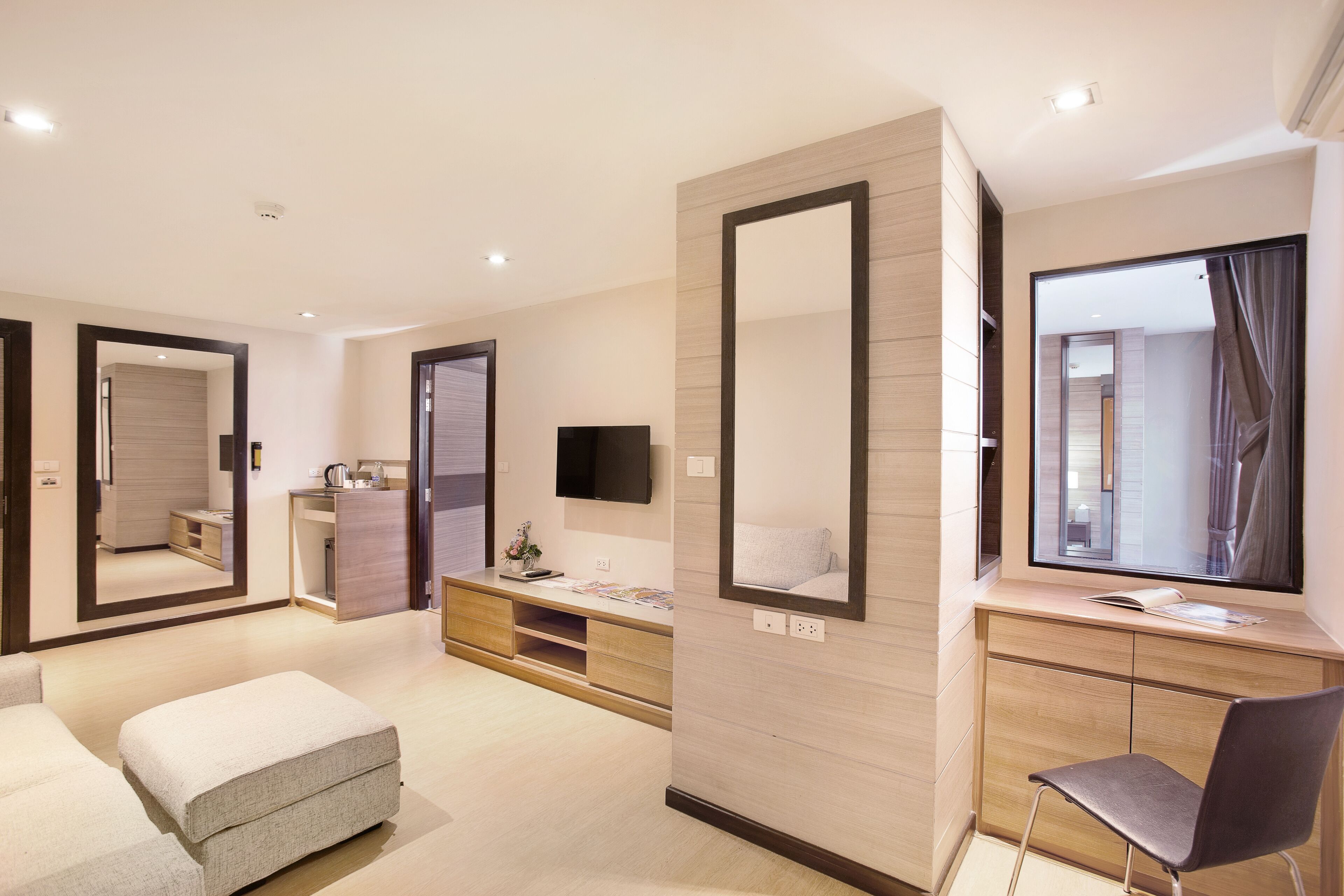 A modern hotel room with a large mirror, a flat-screen TV, a wooden vanity, and a comfortable seating area.