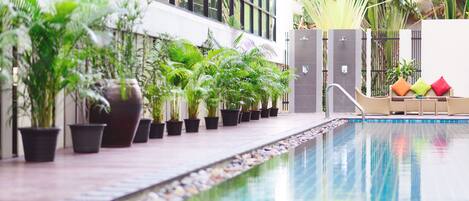 A swimming pool with potted plants and a seating area with cushions.