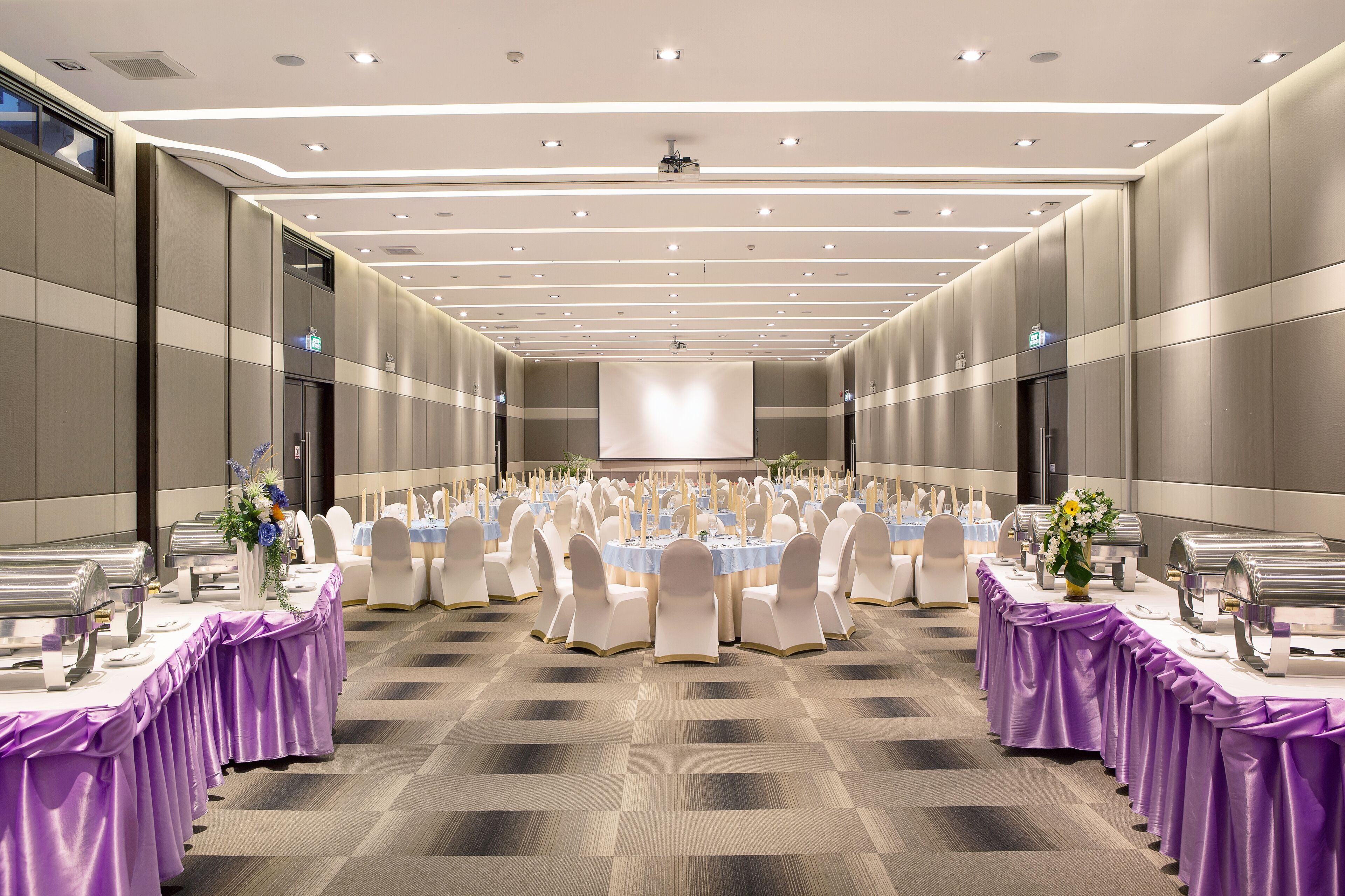 A large banquet hall with rows of round tables, each with a purple tablecloth and white chairs.