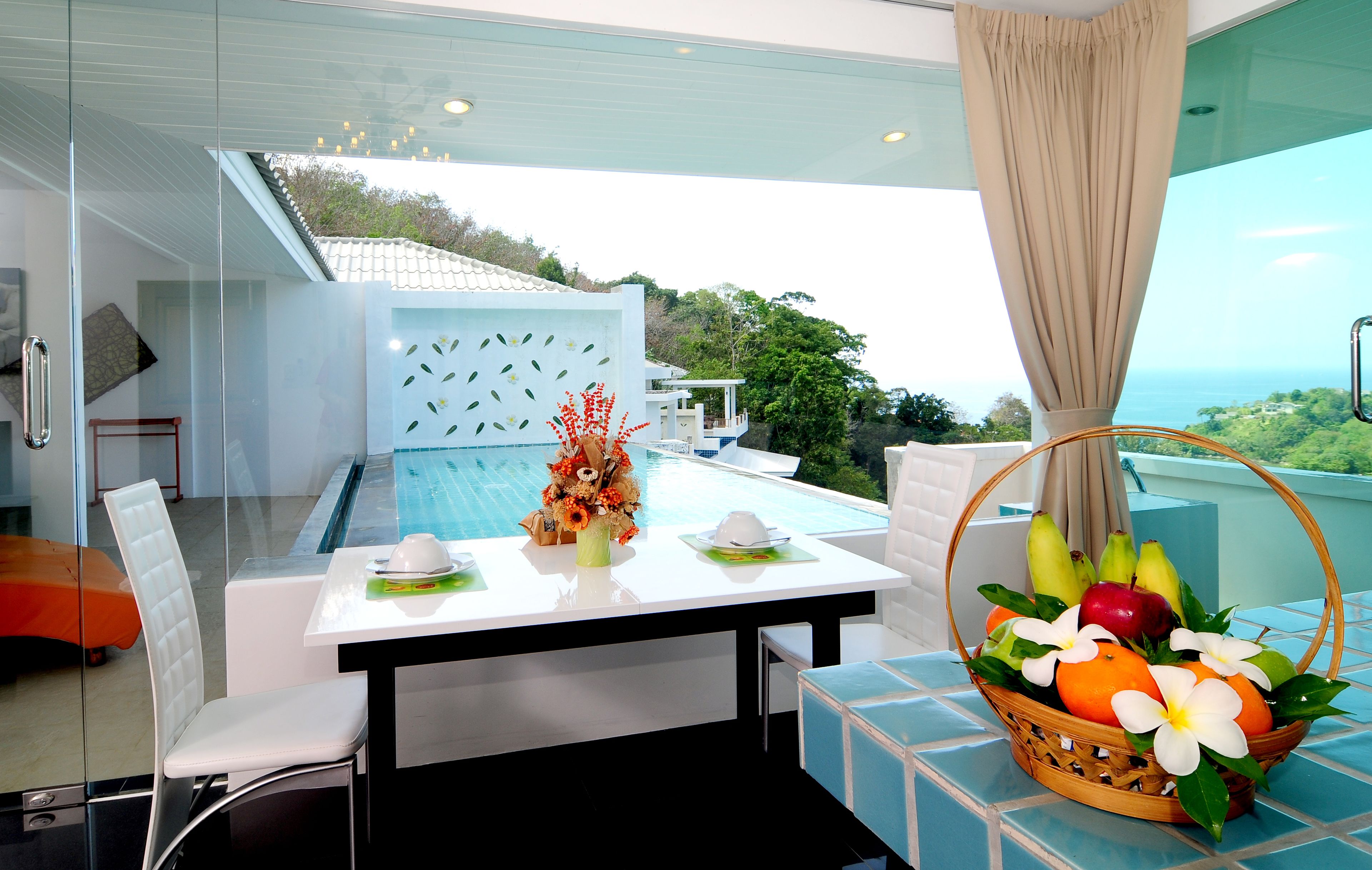 A modern dining area with a pool view, a dining table with a fruit basket, and a white chair.