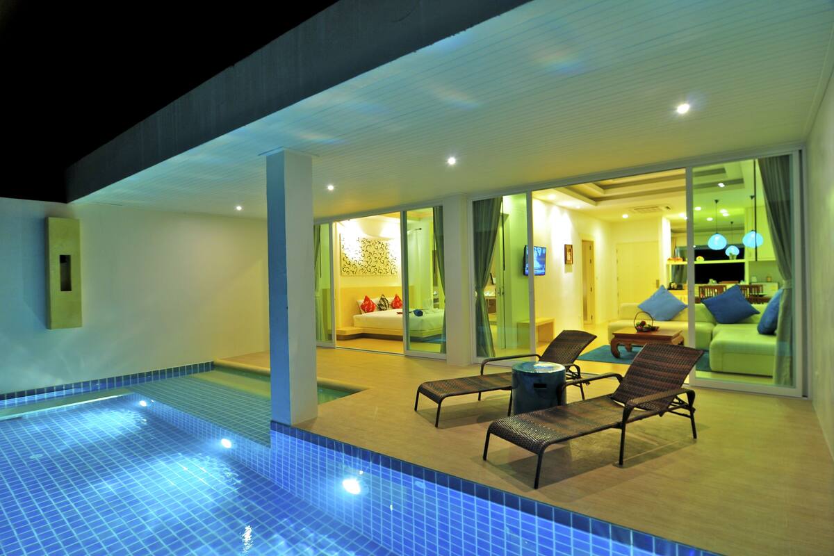 A modern hotel with a swimming pool, lounge chairs, and a well-lit interior.