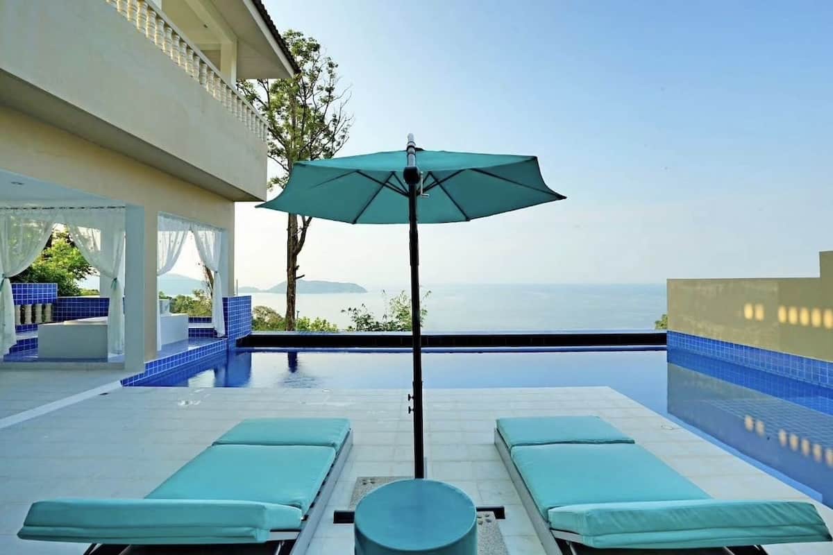 A pool area with lounge chairs and an umbrella, overlooking a body of water.