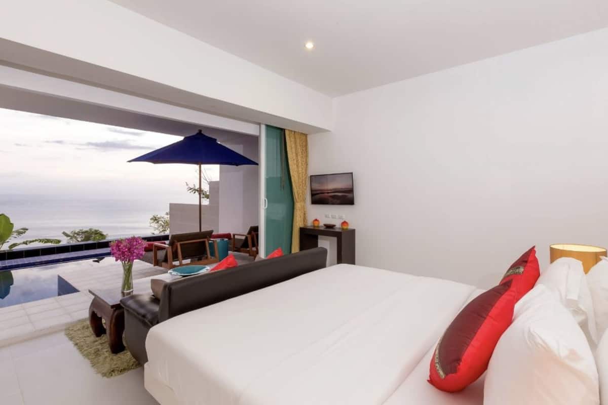 A modern hotel room with a large bed, a desk, and a view of the ocean.