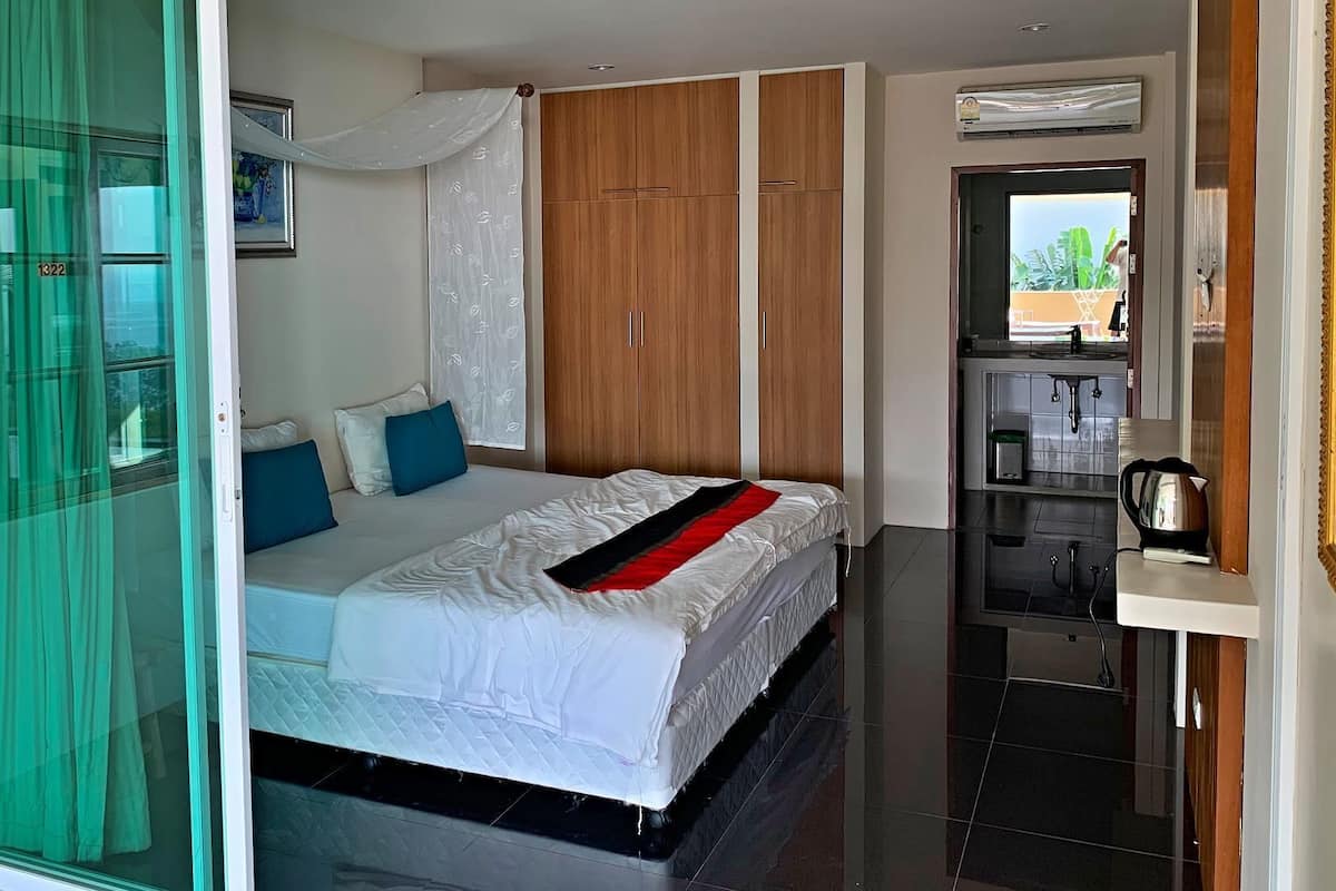 A bedroom with a bed, a wardrobe, a kitchenette, and a sliding glass door.