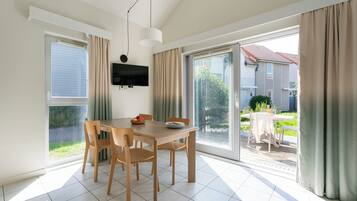 A dining area with a table and chairs, a TV mounted on the wall, and a sliding glass door leading to an outdoor patio.