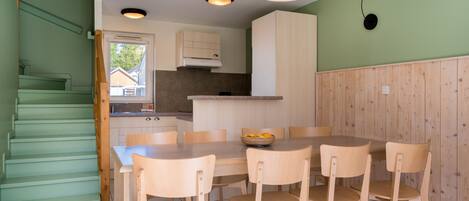 A modern kitchen with wooden cabinets, a dining table with chairs, and a staircase with green walls.