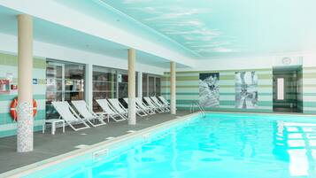 Une piscine intérieure dotée de chaises longues et d’un mur carrelé orné de tableaux.