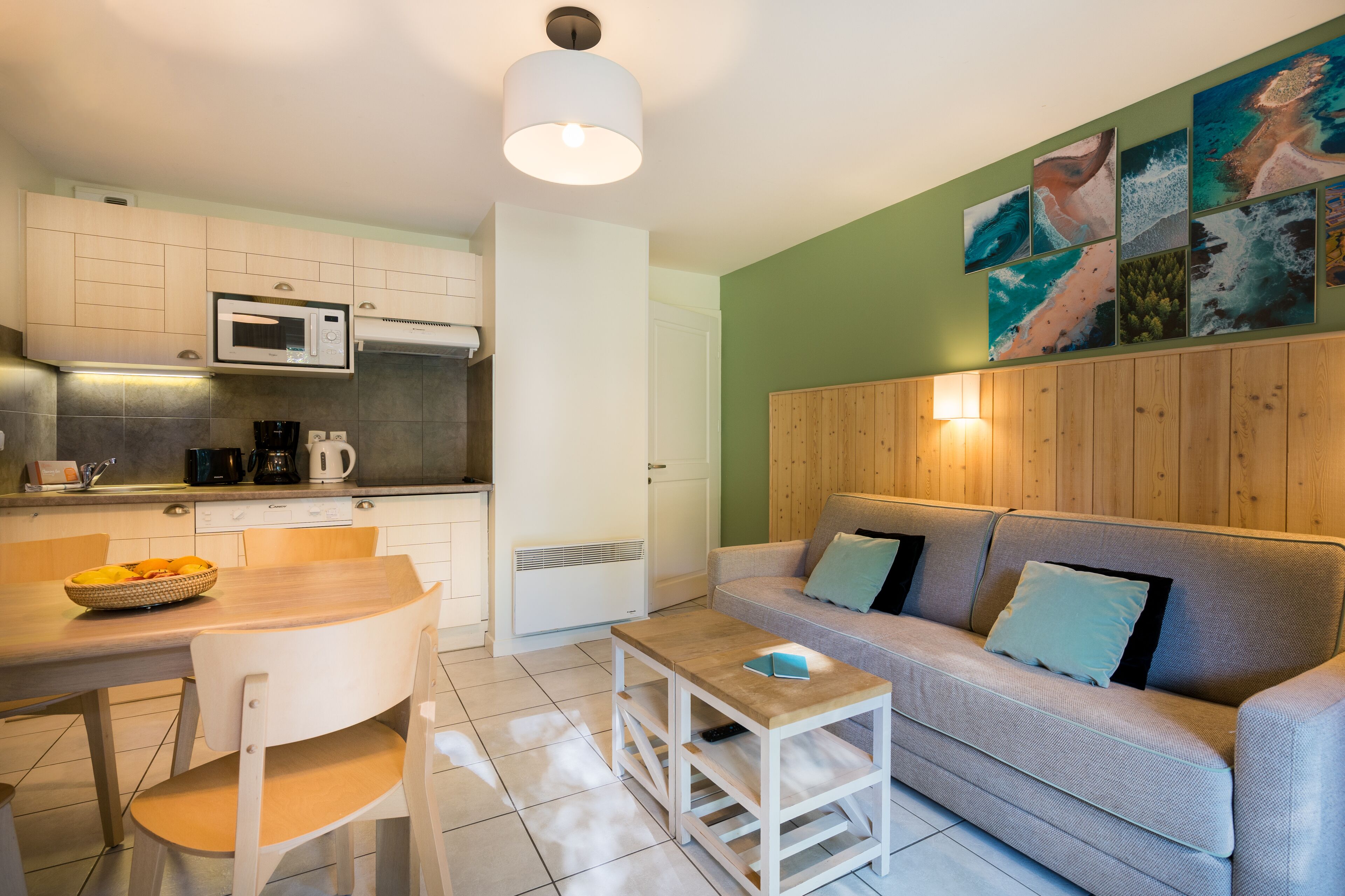 Una cocina moderna con microondas, cafetera y un tazón de fruta en la encimera. Hay una mesa de comedor de madera con sillas y un sofá con cojines en la sala de estar.