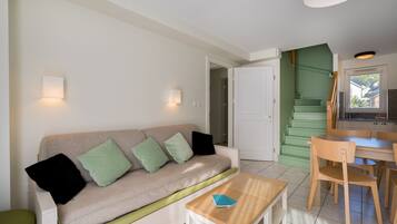 Ein modernes Wohnzimmer mit einem beigen Sofa, grünen Kissen, einem Holztisch und einer Küchenzeile mit einer grünen Treppe.