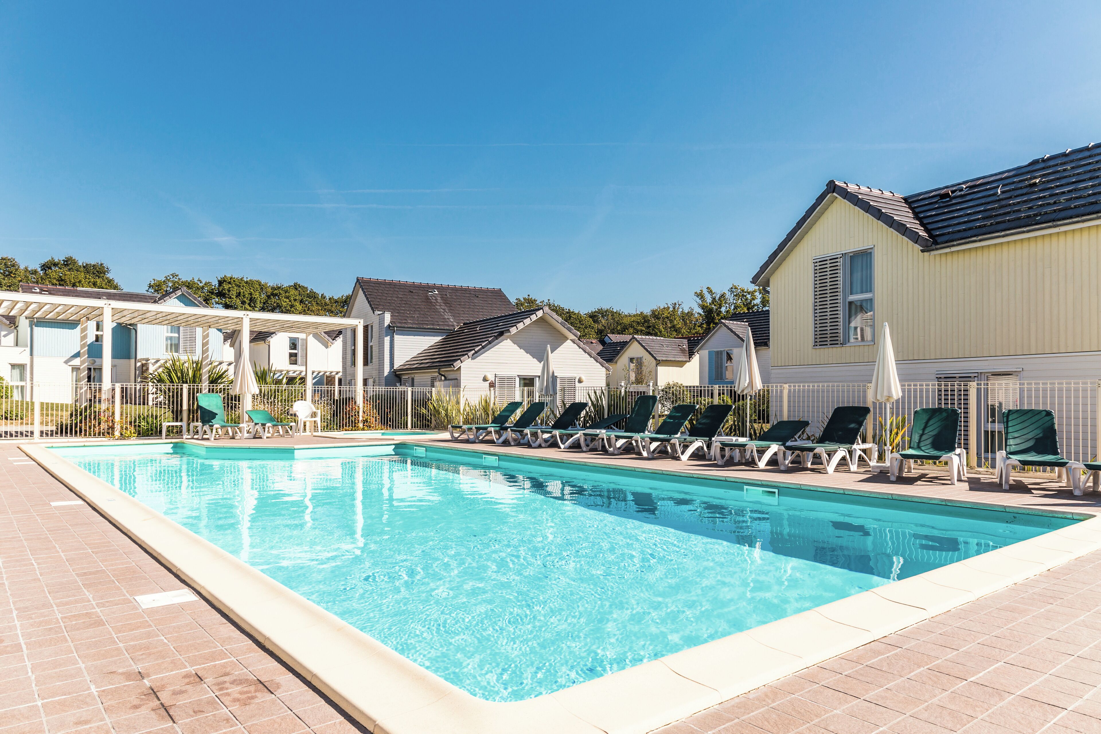 Ein Schwimmbecken mit Liegestühlen und einem überdachten Bereich, umgeben von Gebäuden.