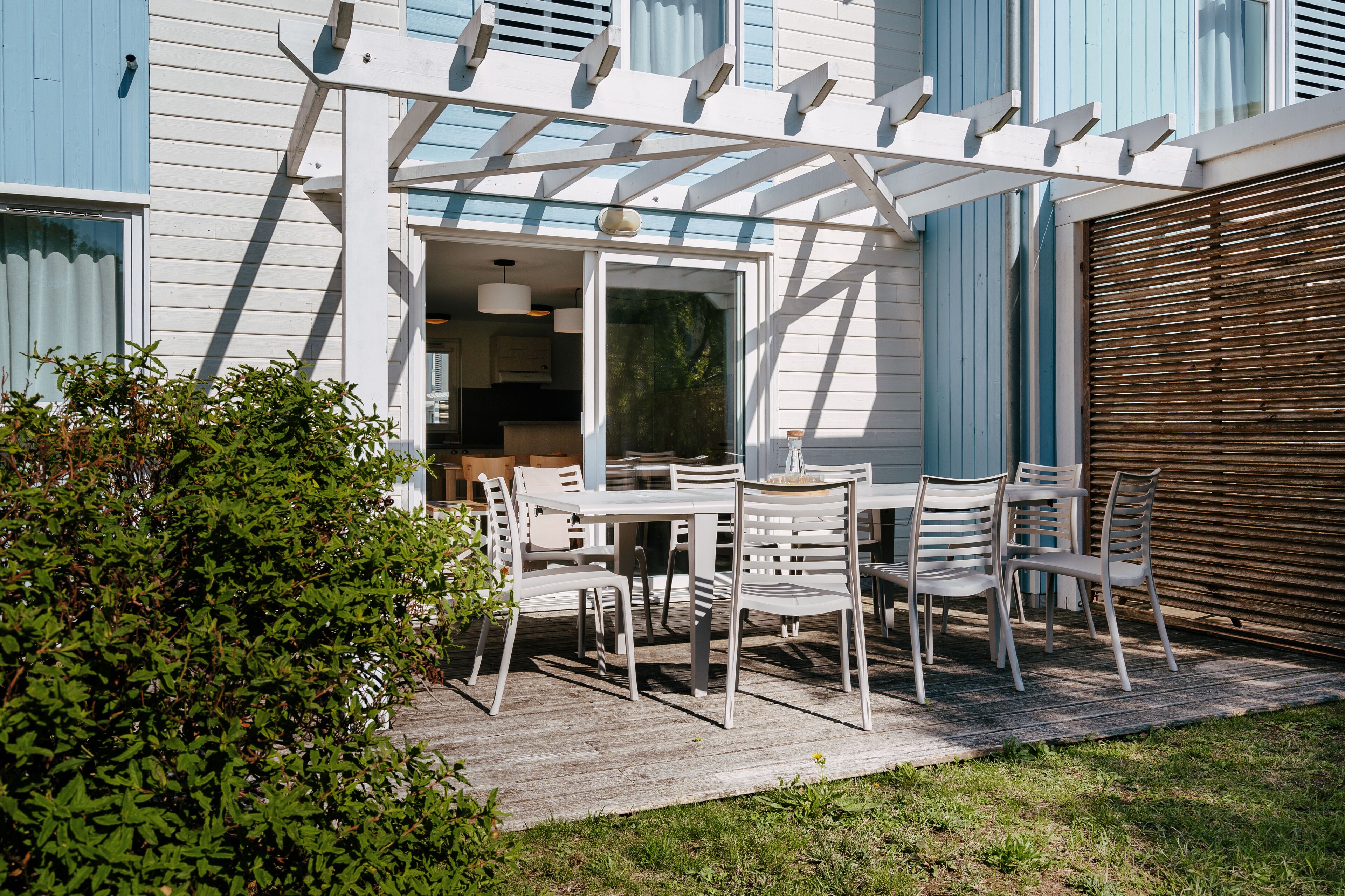 En uteplats med utemöbler, en pergola och utsikt över husets interiör.
