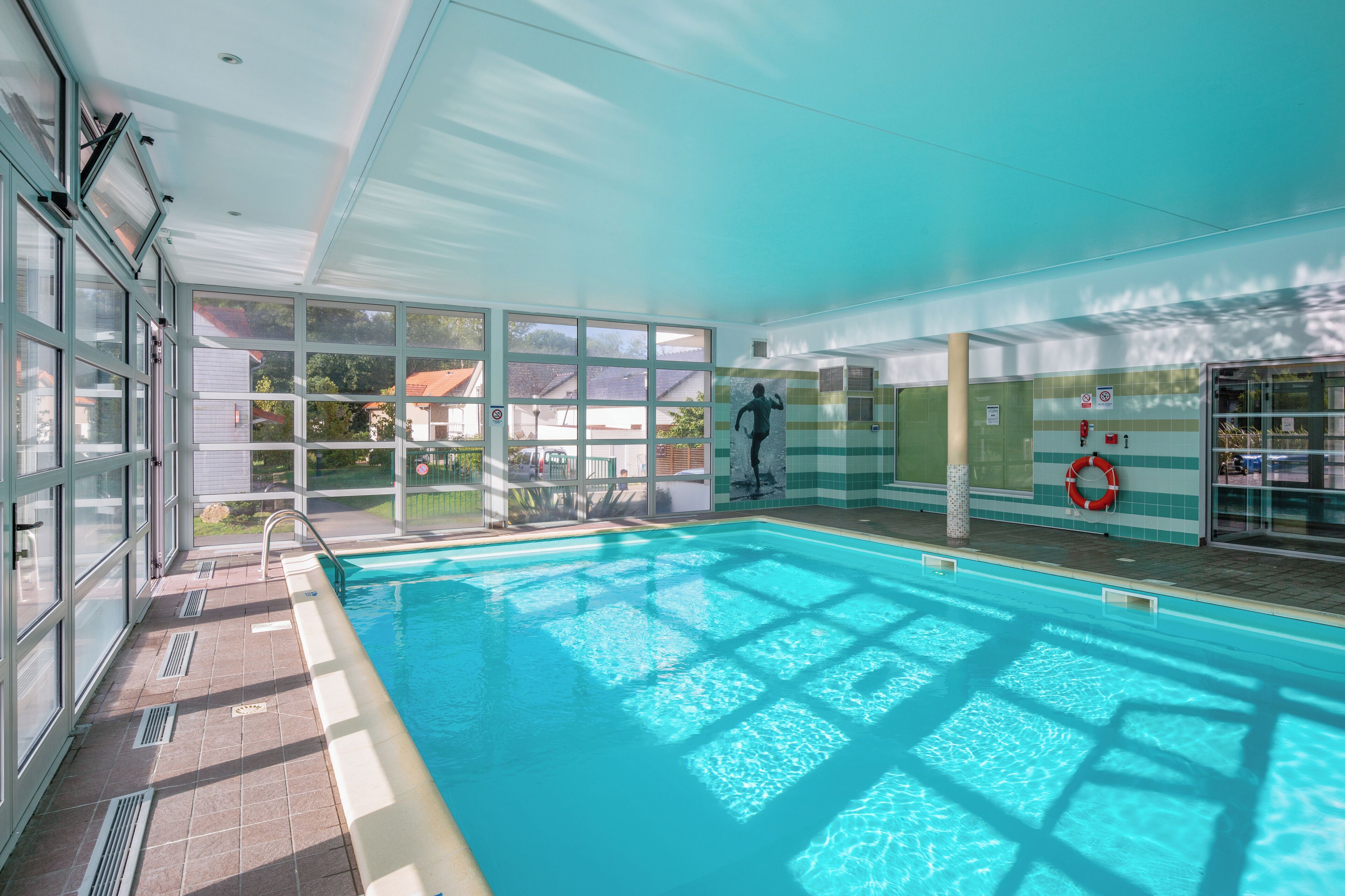 Une piscine à l’eau d’un bleu cristallin, de grandes fenêtres et une bouée de sauvetage accrochée au mur.