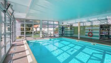 Una piscina con agua azul cristalina, ventanas amplias y un flotador en la pared.