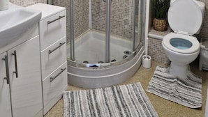 A modern bathroom with a glass-enclosed shower, white tiled walls, a white sink, and a toilet with a blue tank.