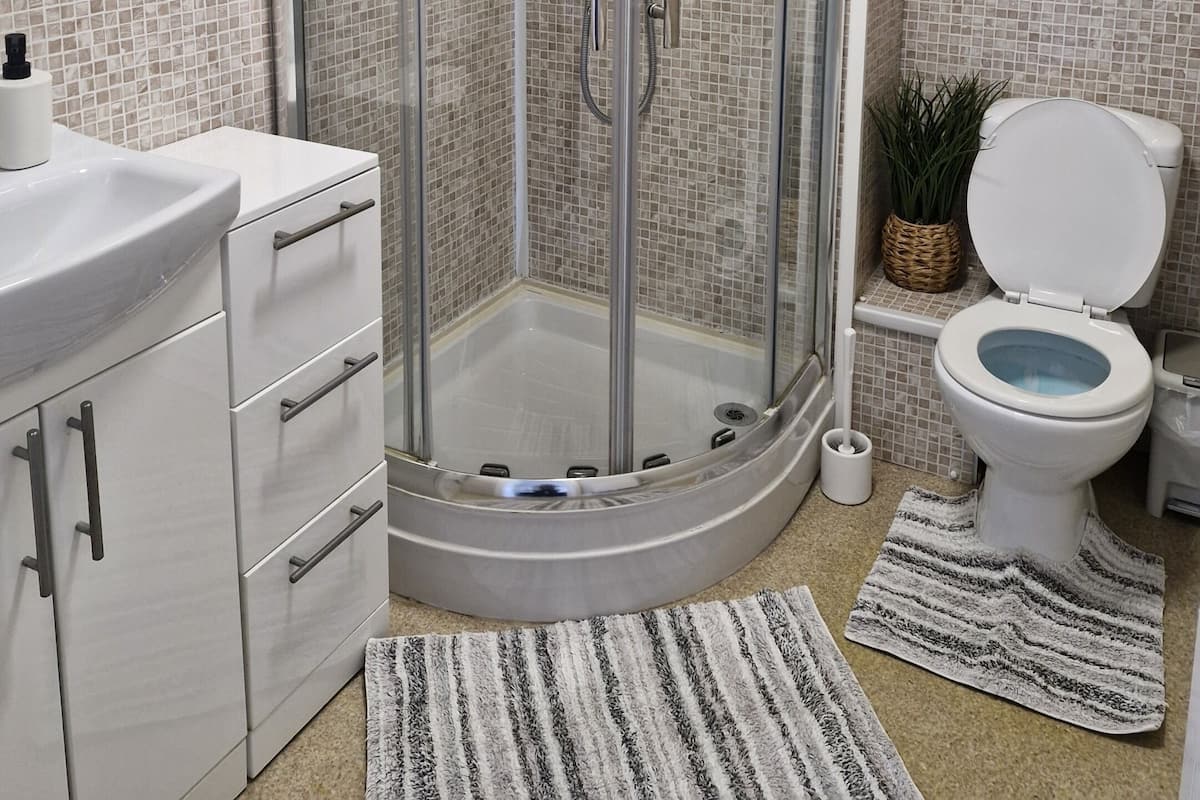 Une salle de bain moderne avec une douche à parois de verre, des murs recouverts de carreaux blancs, un lavabo blanc et des toilettes avec une cuvette bleue.