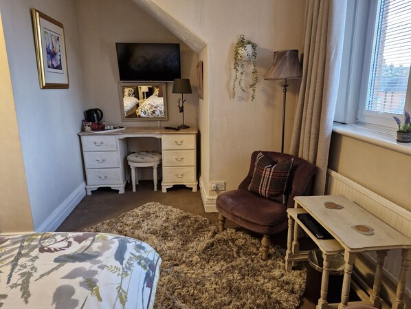 A bedroom with a bed, a desk, a chair, a TV, and a window with curtains. - Warwick Lodge Guesthouse (Carlisle)