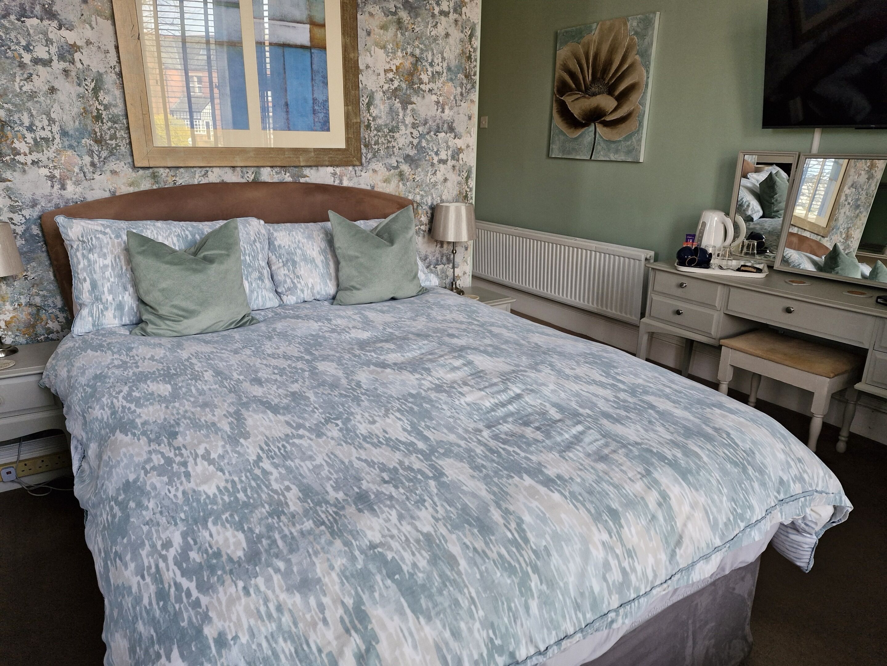 A bedroom with a bed, bedside table, dresser, mirror, and a wall-mounted flower decoration.