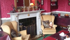 A traditional living room with a fireplace, two armchairs, a table set for dining, and a bookshelf.
