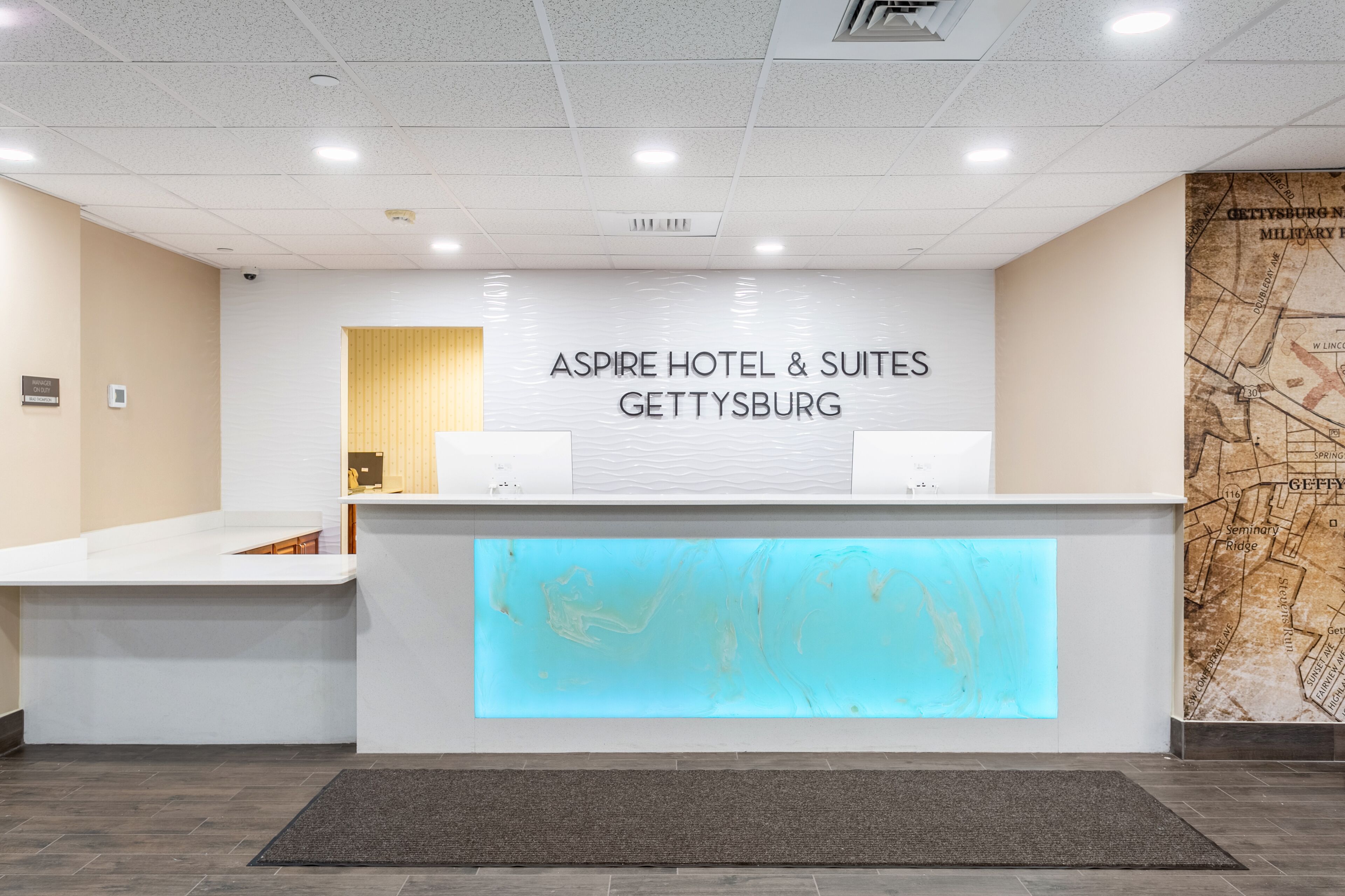 A reception desk with a modern design, a map on the wall, and a sign for Aspire Hotel & Suites in Gettysburg.